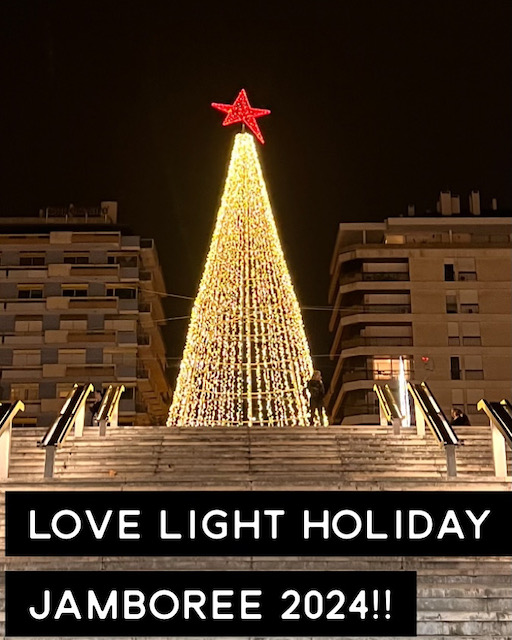 A brightly lit Christmas tree is silhouetted against a dark night sky. Across the bottom of the photo are the words "LOVE LIGHT HOLIDAY JAMBOREE 2024!!".