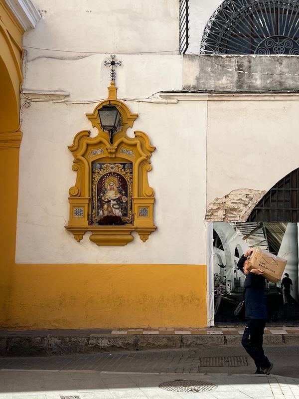 A photo of a man walking down a sloping street, carrying a heavy box marked "Made in China".